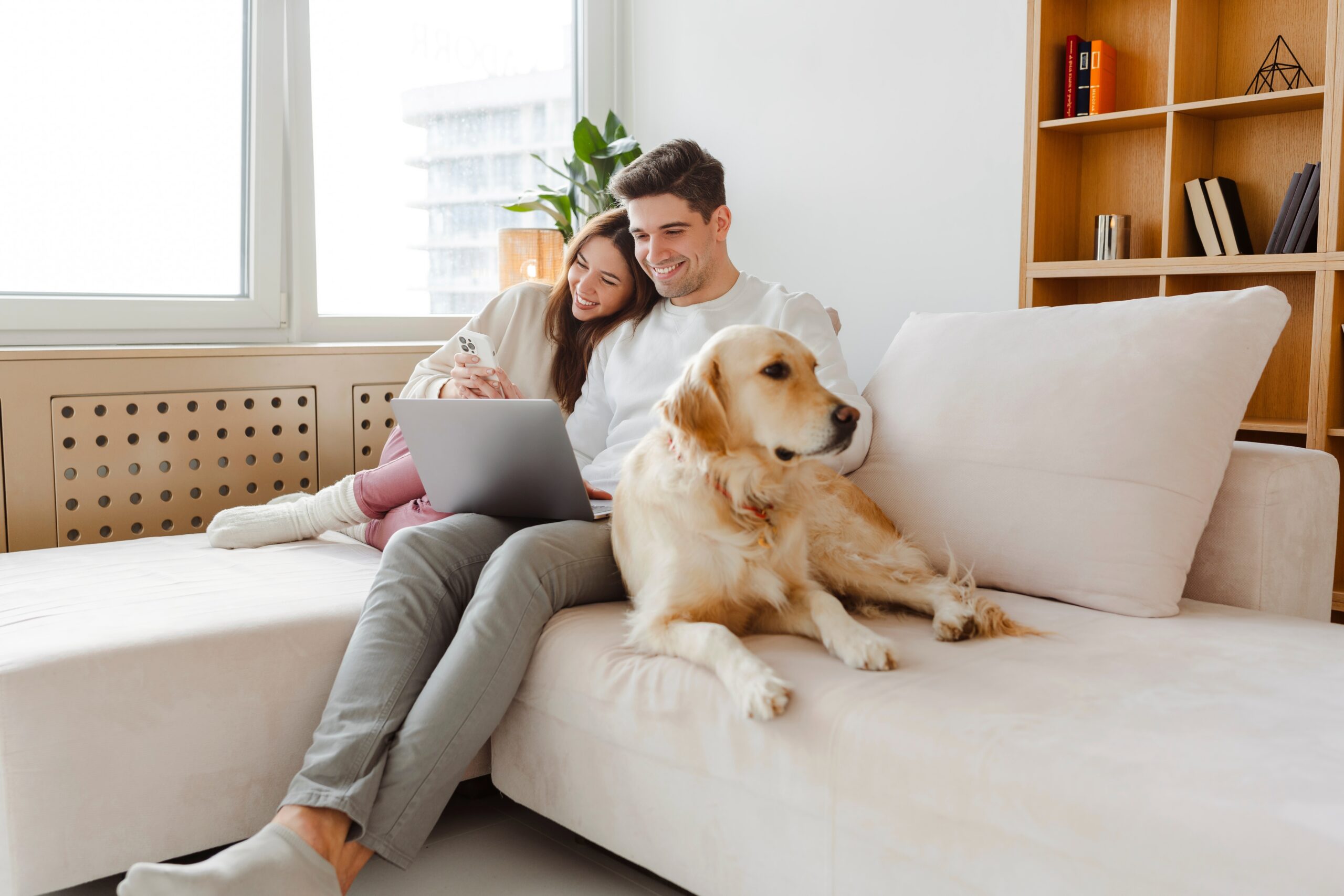 young happy couple on the couch with laptop and dog